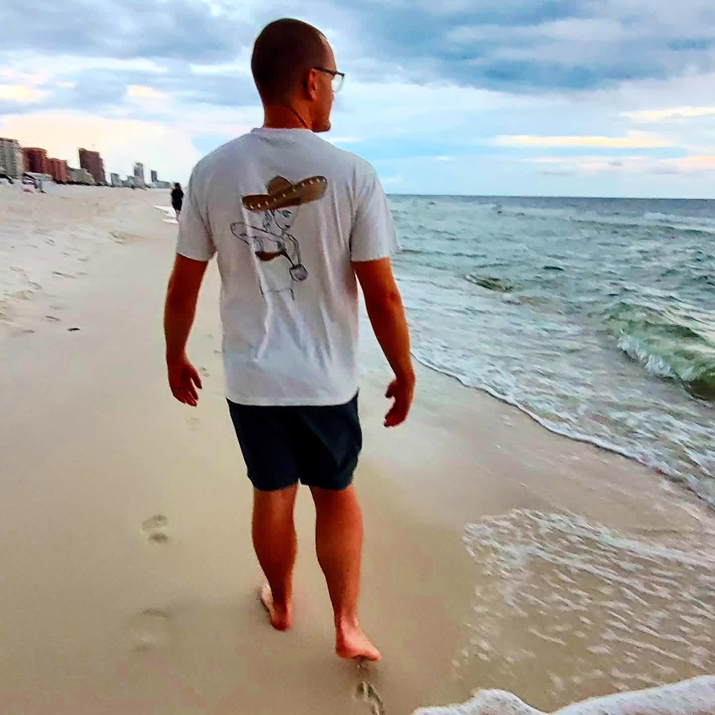 2025-09-25 1838 hours - Brady walks down the Beach wearing his El Cafecito Tee Shirt in Orange Beach